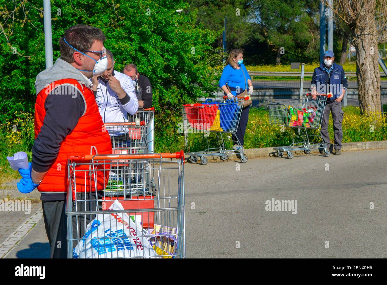 Crowd of italian white people waiting hours in line outside a grocery store with shopping carts and coronavirus masks to buy essentials. Routine and s Stock Photo