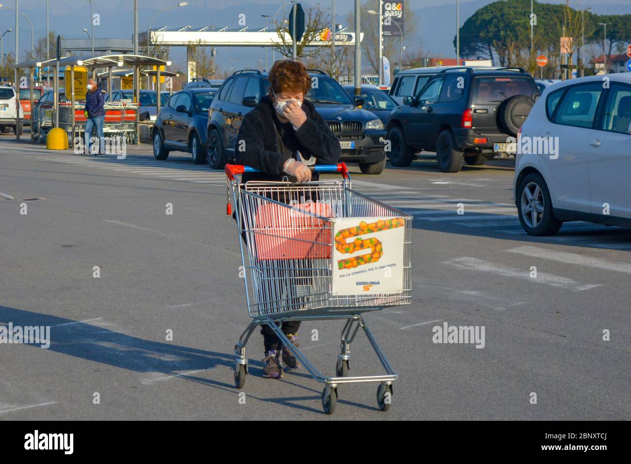 Tuscany, Italy 03/21/20: Routine daily scene during coronavirus national lockdown: a woman with COVID-19 protective mask pushing shopping cart crying Stock Photo