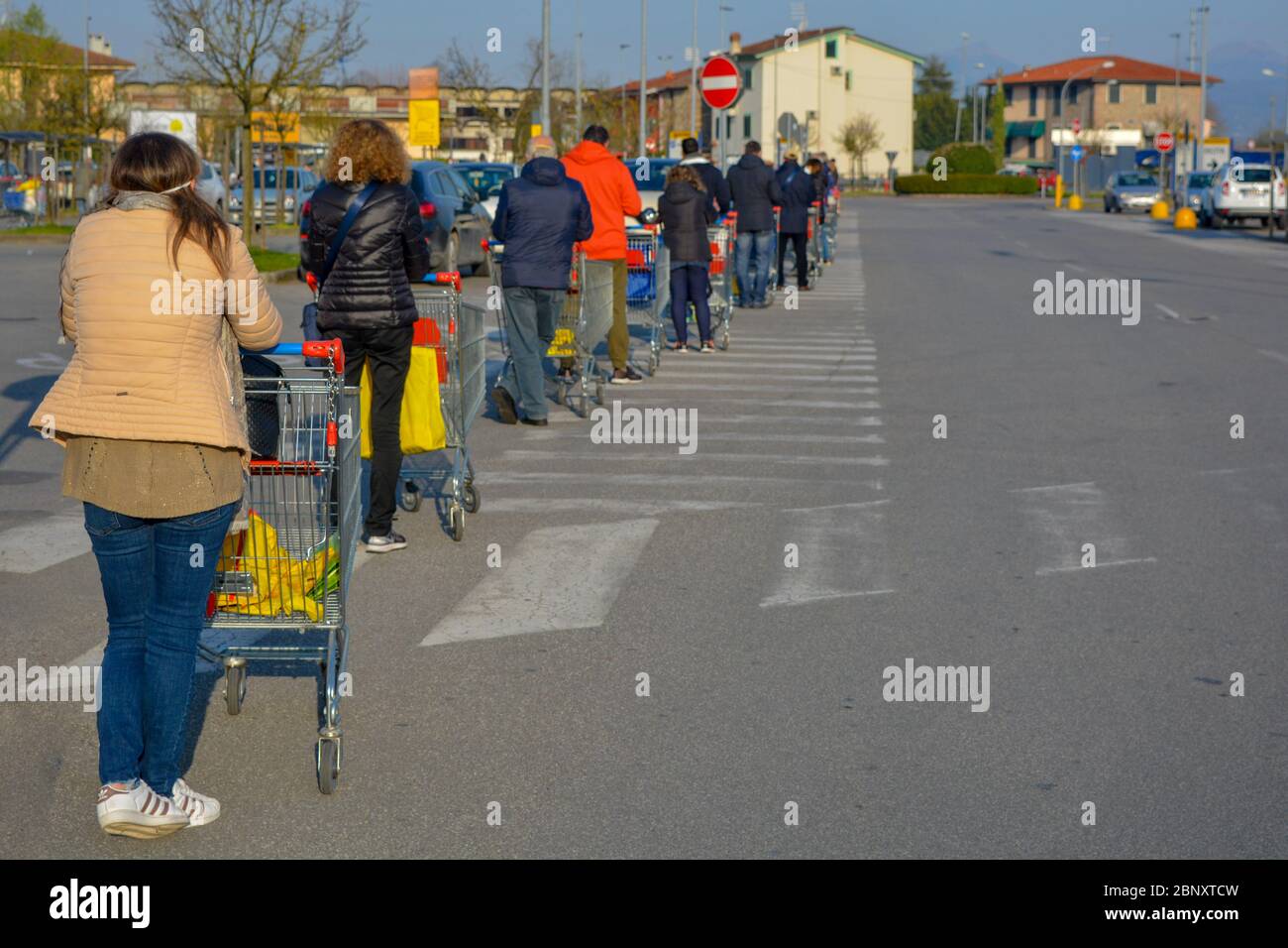 Line of  men and women with COVID-19 protective masks waiting with shopping carts to buy essentials. Stress, tension and social distancing in pandemic Stock Photo