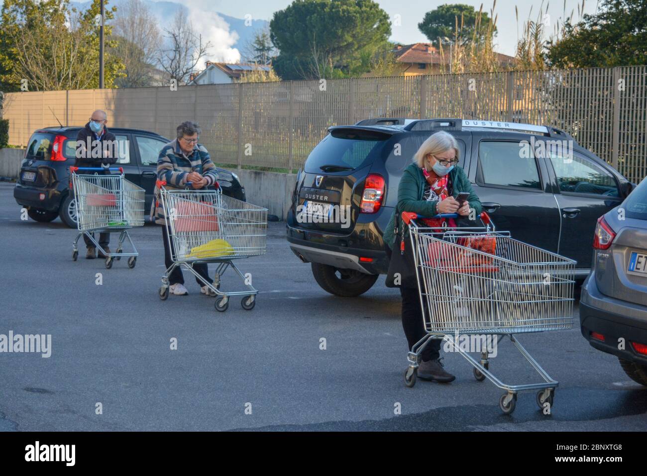 Three italian white men and women with empty shopping carts and coronavirus protective mask have a long waiting time to stockpile essentials. Covid19 pandemic Stock Photo
