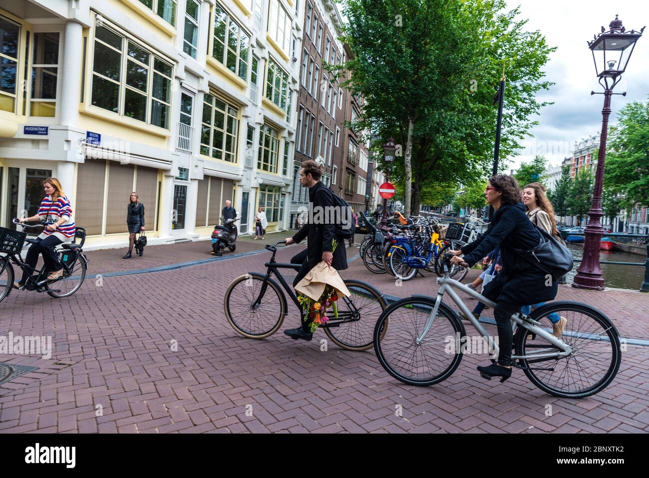 Amsterdam, Netherlands - September 8, 2018: Street with a a young man carrying a bouquet of flowers and more people on bicycle in the old town of Amst Stock Photo