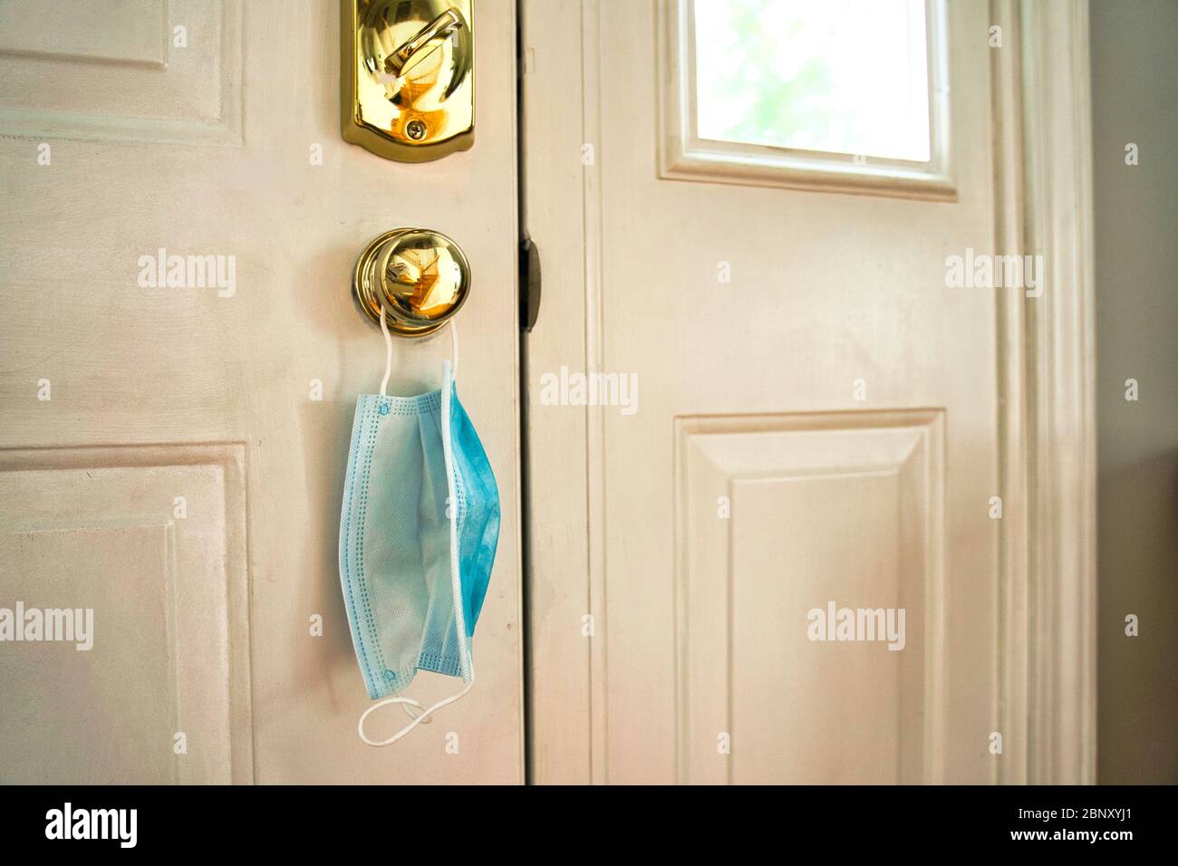 Face mask hanging from door handle on white door with sunlight coming ...