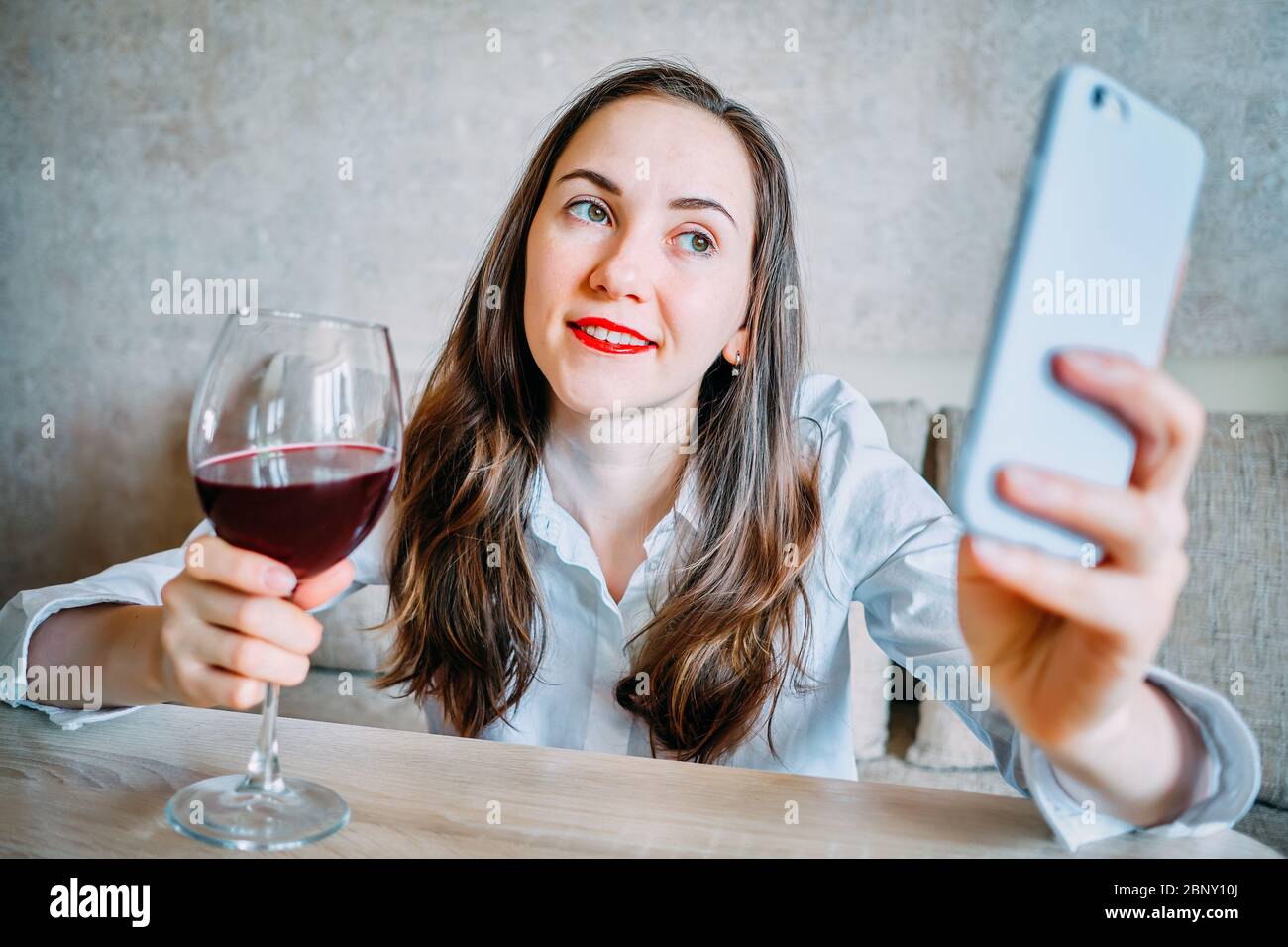 Girl drinks wine on the couch and takes selfie pictures on a smartphone. Close up. Stock Photo