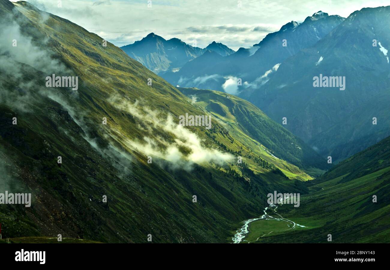 view over green Taschachbach valley towards Pitztal valley with green meadows, clouds and high mountains in the background Stock Photo