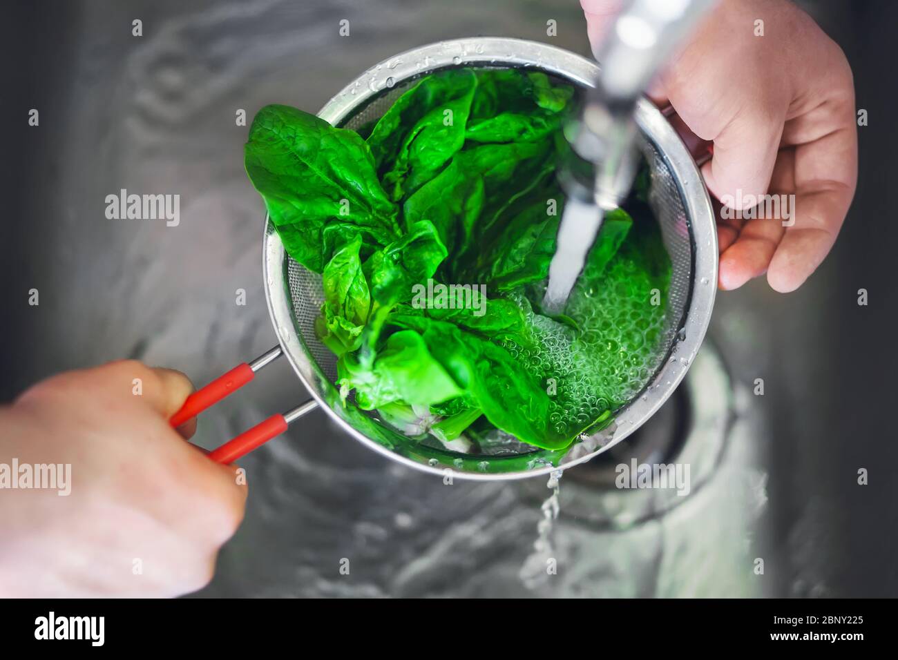 A man is holding a colander with a red handle, in which he washes fresh