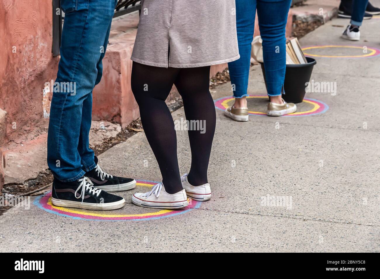 Customers line up at safe distance in front of a store, helped by marks painted on the ground, during coronavirus pandemic Stock Photo