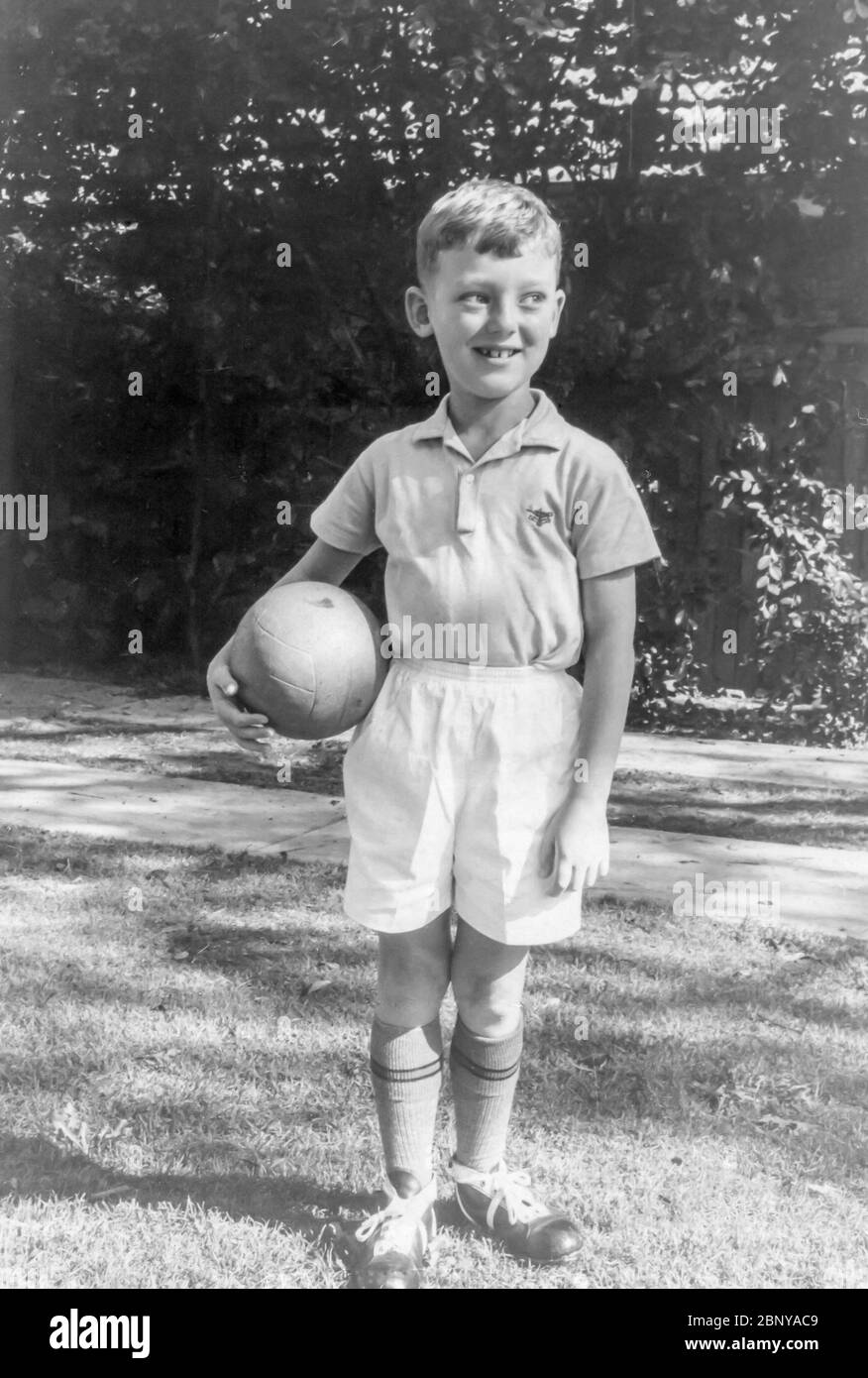 Sydney Australia 1966: A young Australian 6 year old boy stands in his Soccer outfit with a football in the backyard of his Sydney home. There is no uniform evident and it is likely that this boy was headed for pre season trials. Stock Photo