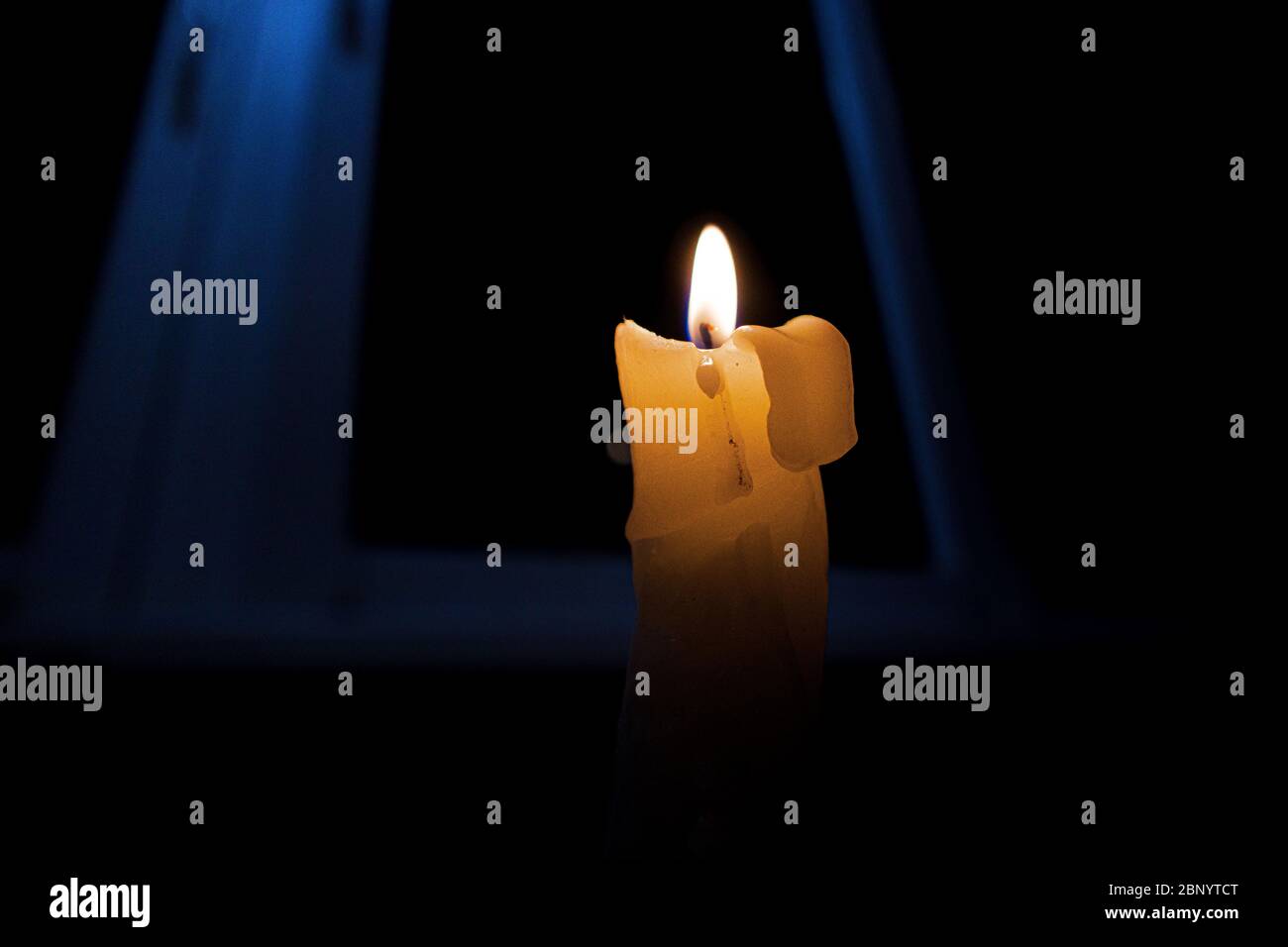 Burning candle in complete darkness, against the background of the window. Stock Photo
