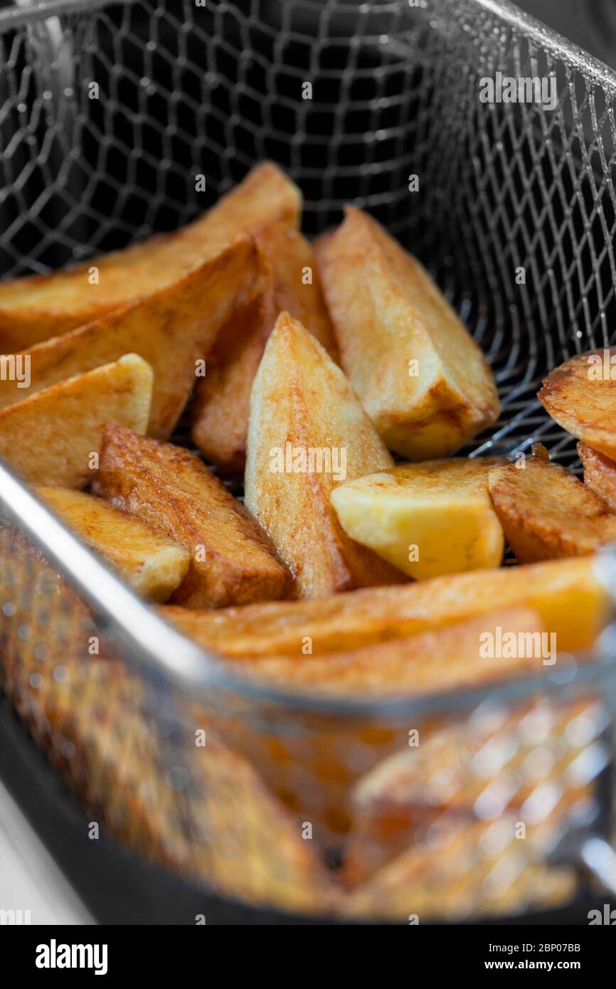 Chips cooking in vegetable oil in a deep fat fryer appliance. Unhealthy