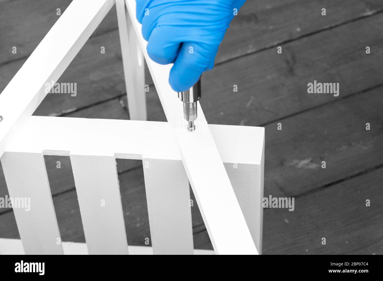 Man assembling a white flat pack ladder shelving unit with a screwdriver.  Flat pack assembly concept Stock Photo