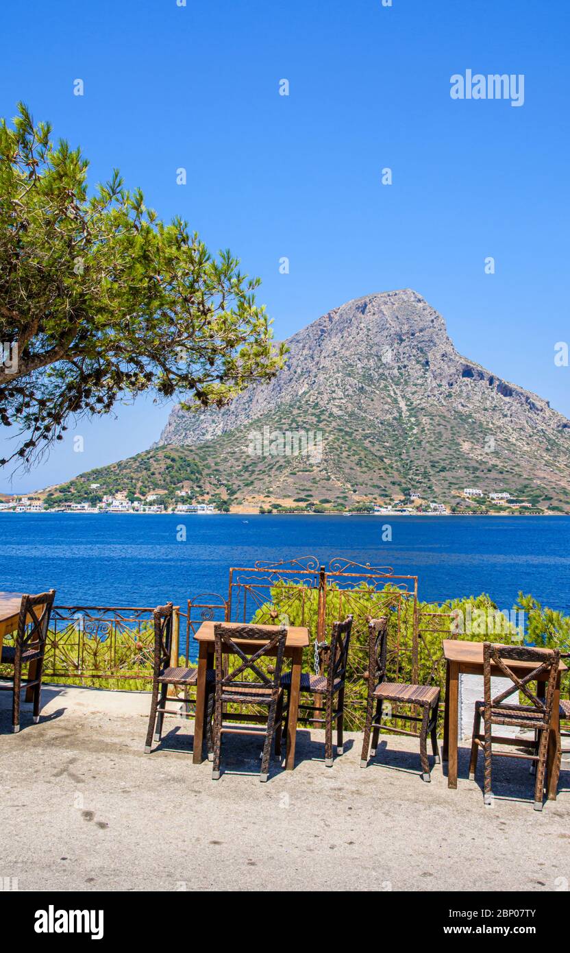 Sea views over road side restaurant table and chairs in the holiday resort town of Mirties, Kalymnos, Dodecanese, Greece Stock Photo