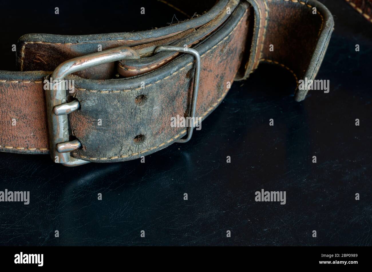 Cracked very old leather belt with a double metal buckle. Closeup of a