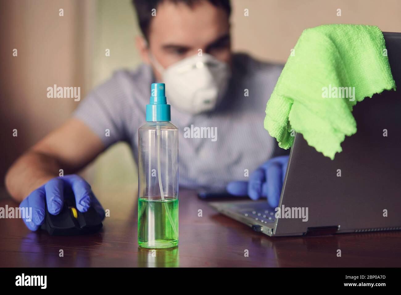 young man wearing medical face mask at work from home office due to corona virus outbreak with laptop on wooden table, remote work against background Stock Photo