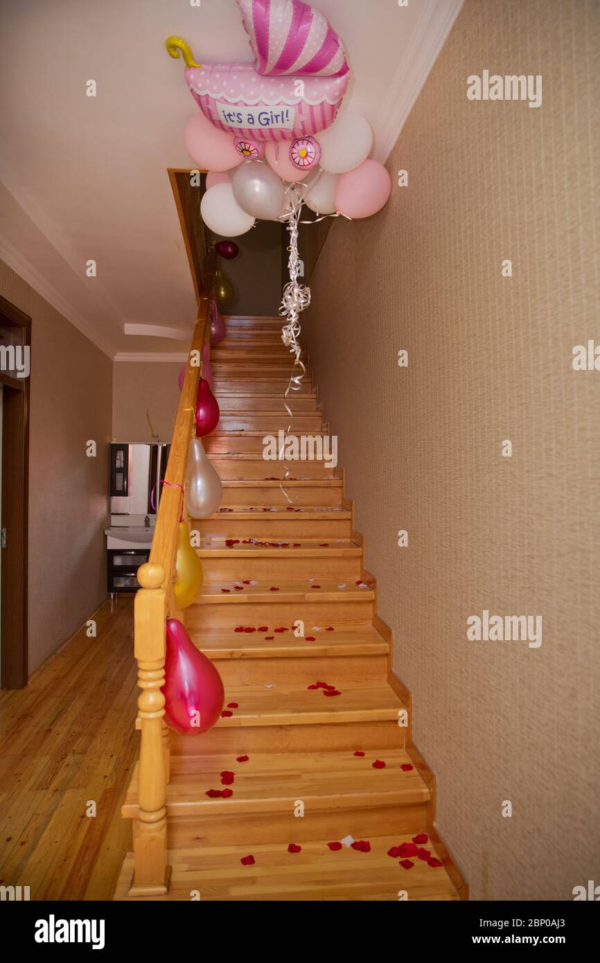 Petals of a red rose on a wooden staircase . Red, yellow, white balloons hanging on the handles of the stairs . Wooden staircase . Stock Photo
