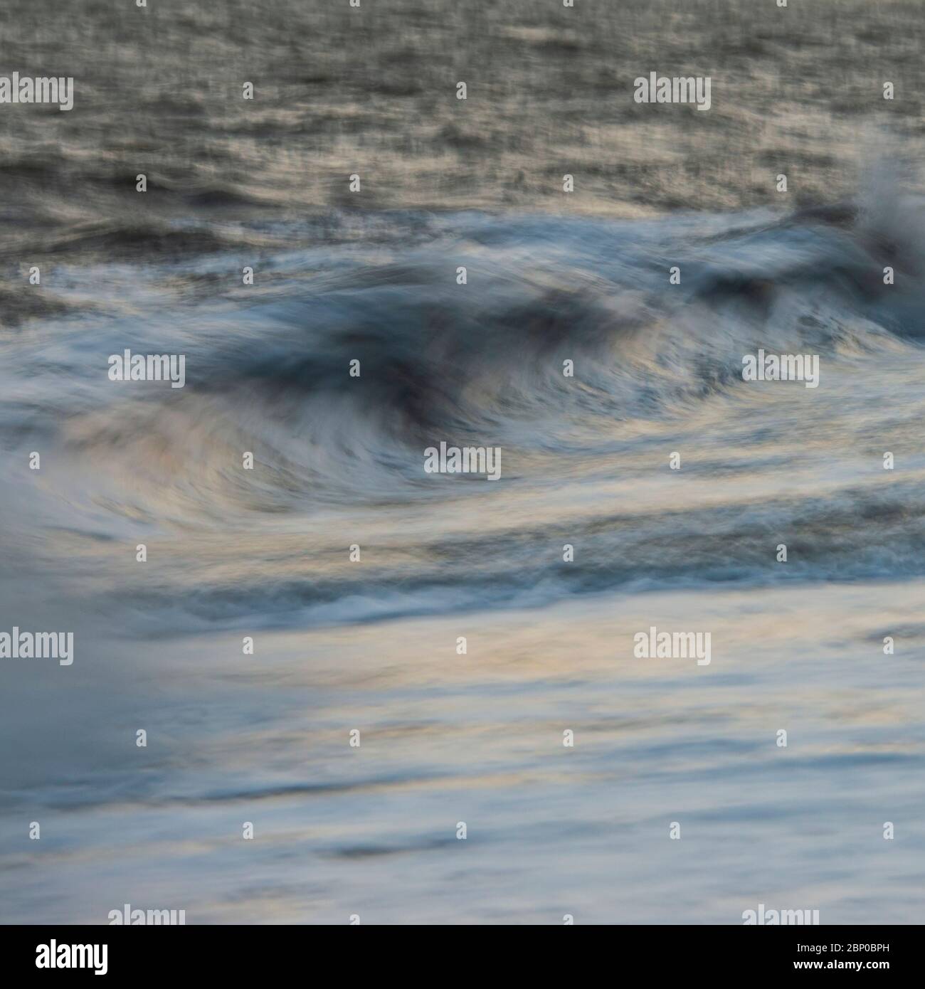 Beautiful abstract long exposure landscape image of waves crashing onto groynes on beach during sunset Stock Photo