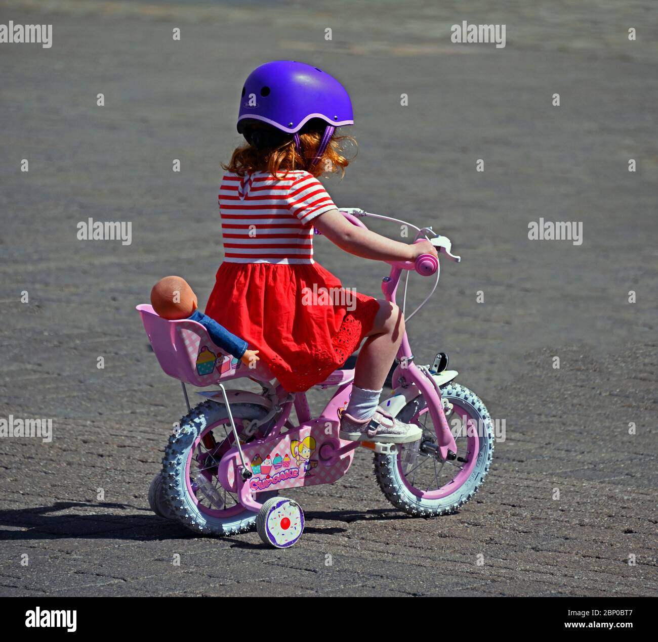 Small girl riding a bicycle with stabilisers. Market Place, Kendal, Cumbria, England, United Kingdom, Europe. Stock Photo