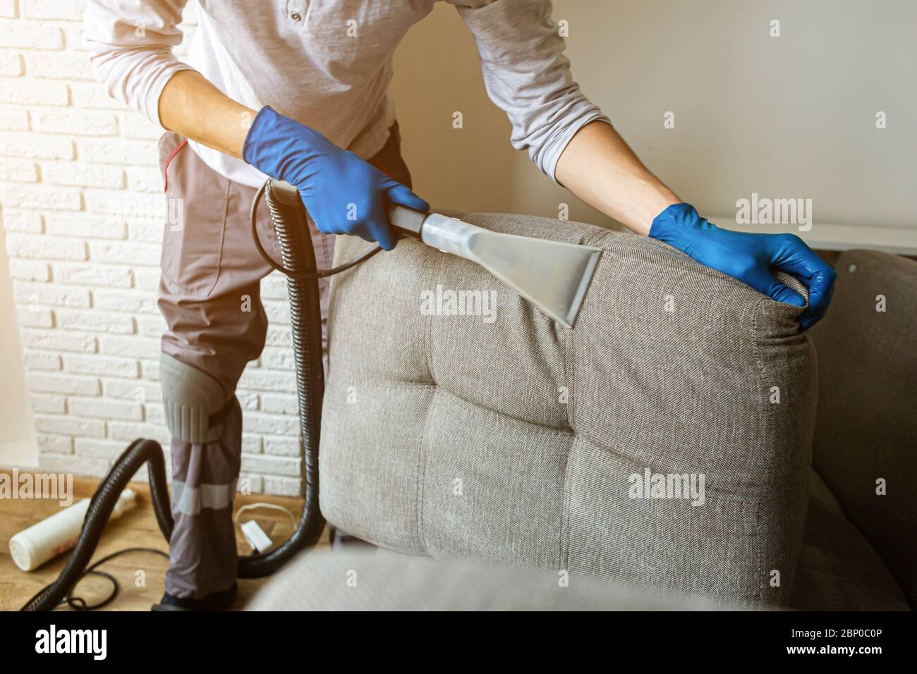 Dry cleaner's man employee removing dirt from furniture in flat, closeup, vacuum clean sofa with