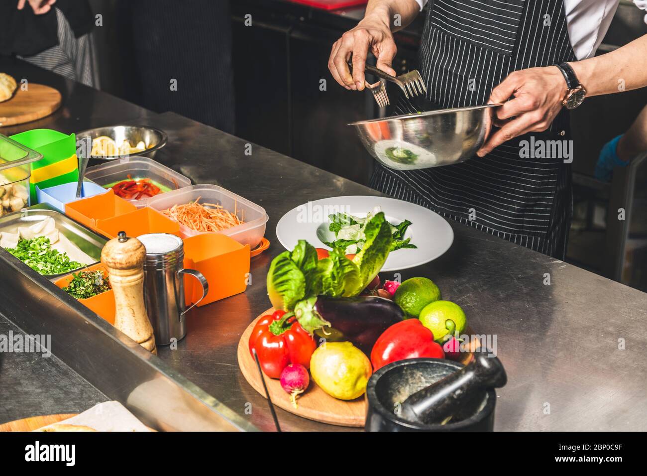 Professional chef cooking in the kitchen restaurant at the hotel, preparing dinner. A cook in an apron makes a salad of vegetables and pizza. Stock Photo