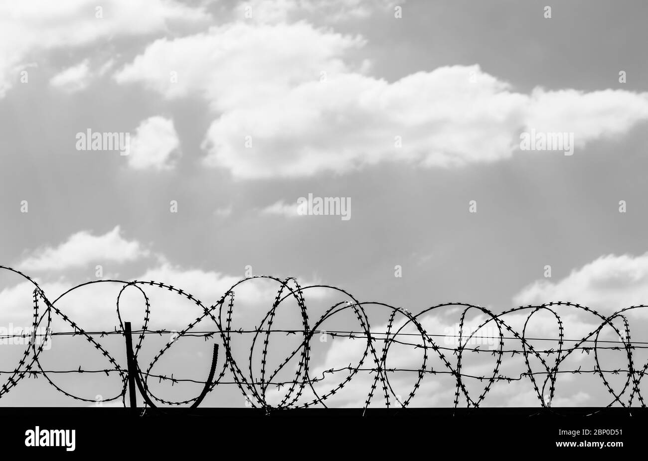 Black coiled barbed wire fence and sky with sunlit clouds at background ...