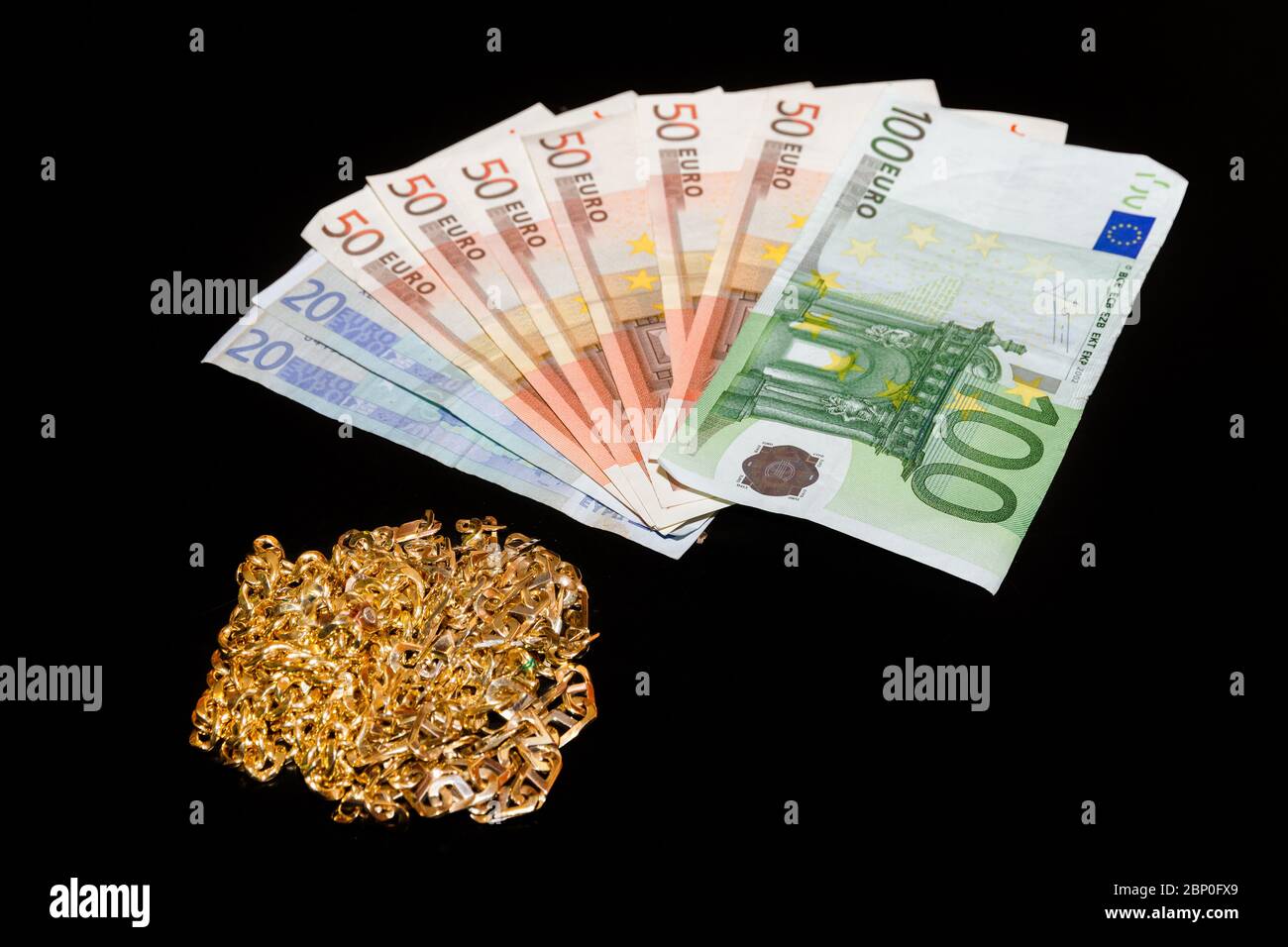 Money and gold jewellery against a black background. Stock Photo