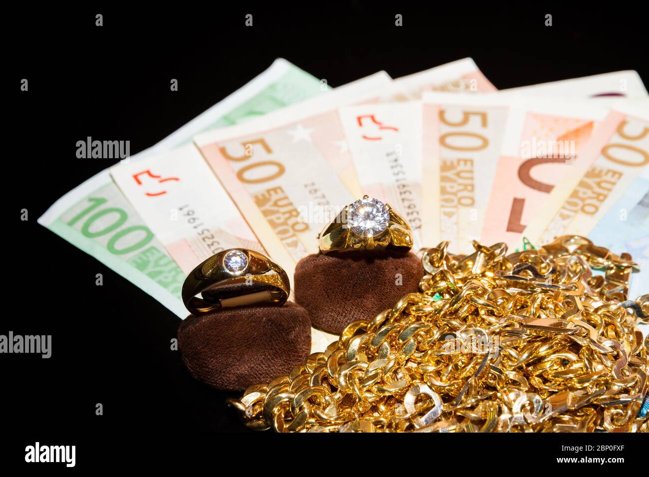 Money and gold jewellery against a black background. Stock Photo
