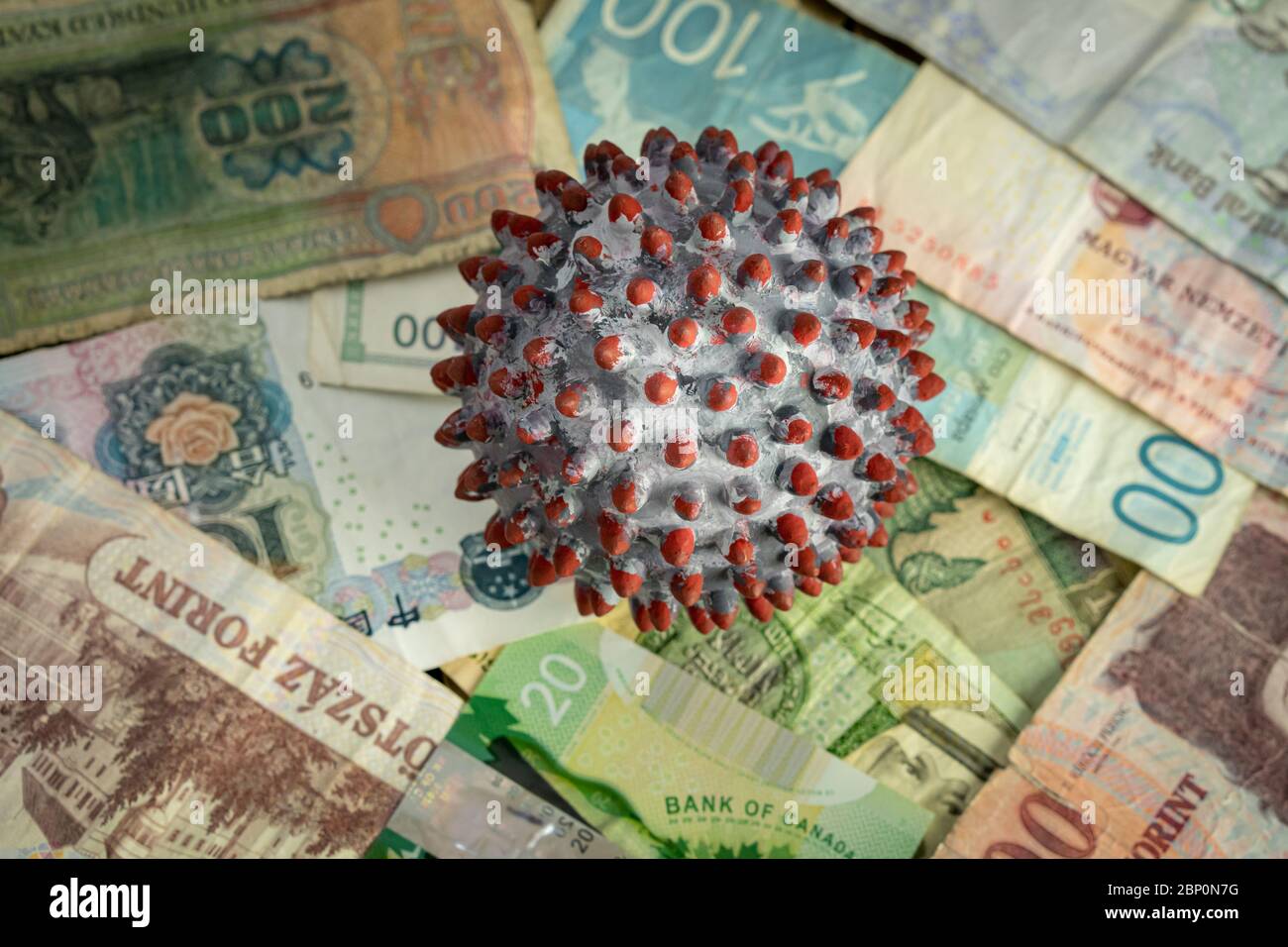 A ball painted like a SARS-CoV-2 virion on the middle of many banknotes from different countries Stock Photo