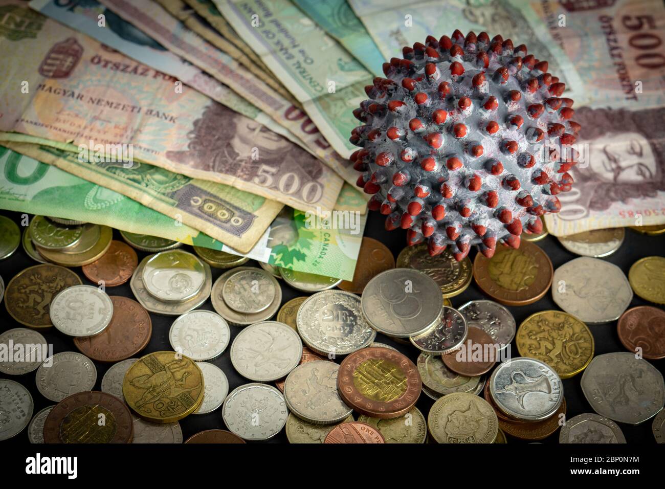 A ball painted like a SARS-CoV-2 virion on the middle of many banknotes and coins from different countries Stock Photo