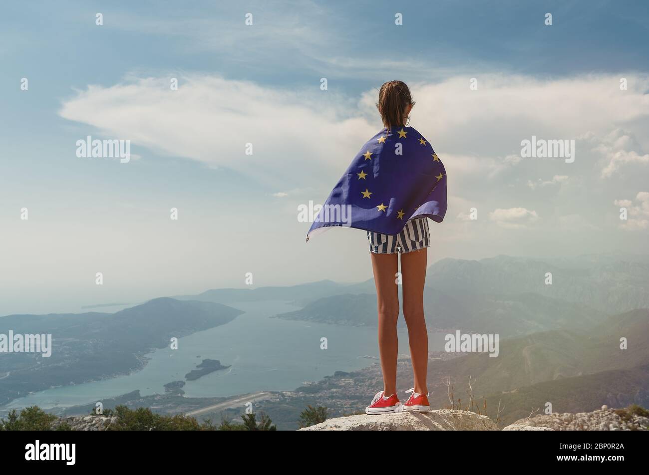 Child teenager girl on the top of the mountain with an European Union flag on her shoulders Stock Photo