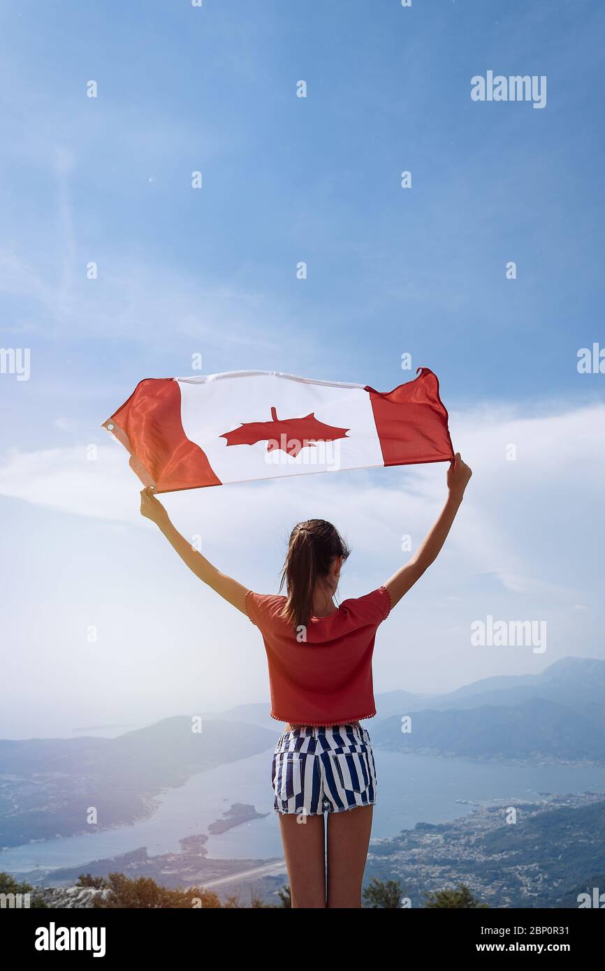 Child girl is waving Canadian flag on top of mountain at sky background
