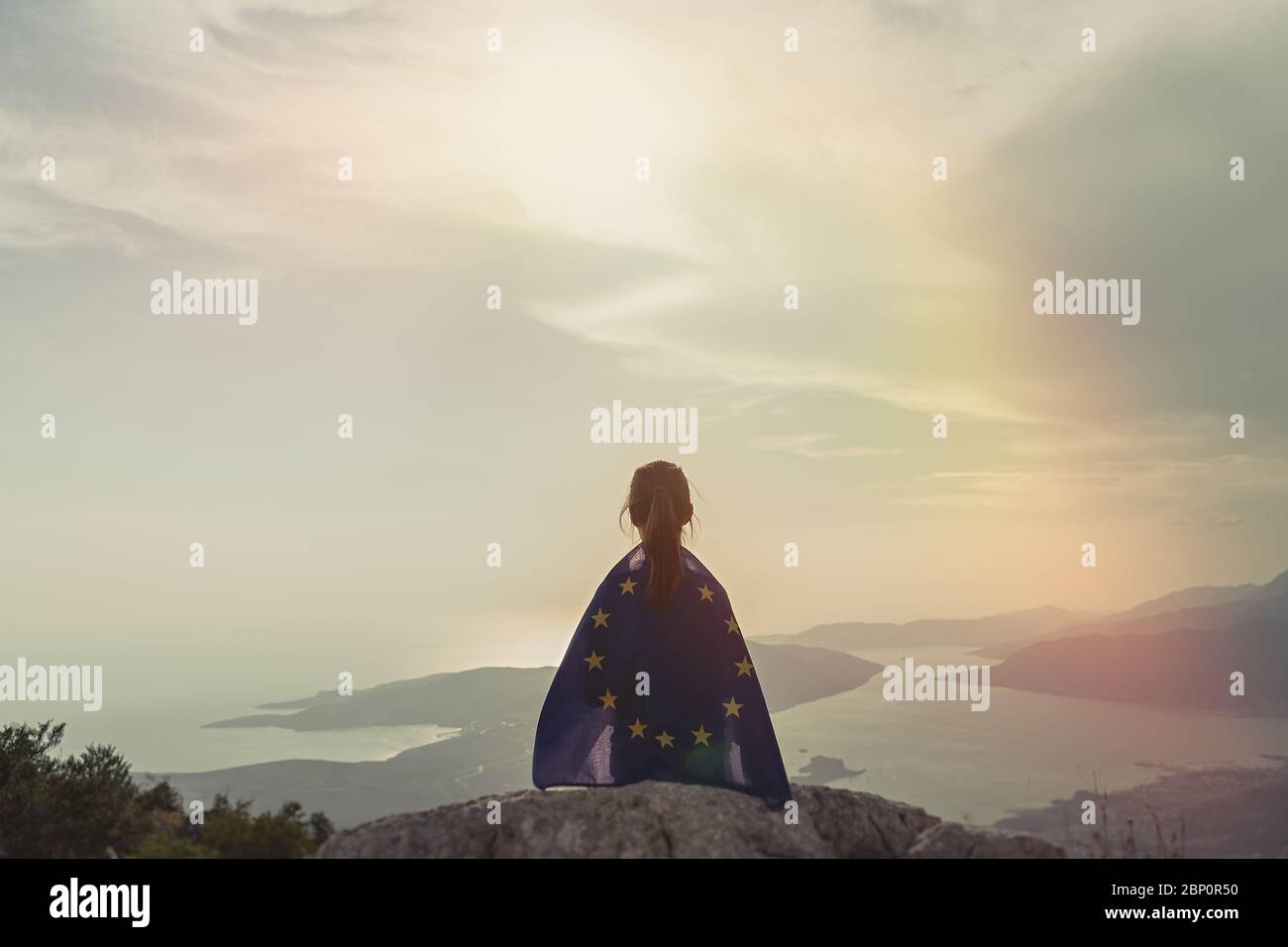 Child teenager girl sitting on the top of the mountain with an European Union flag on her shoulders. Sunset time Stock Photo