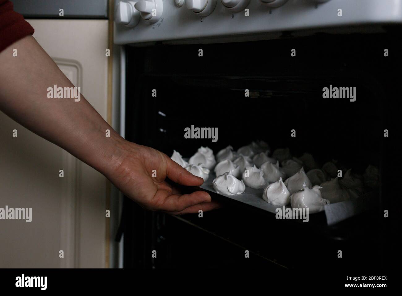 Woman baking white sweet meringues in the oven Stock Photo