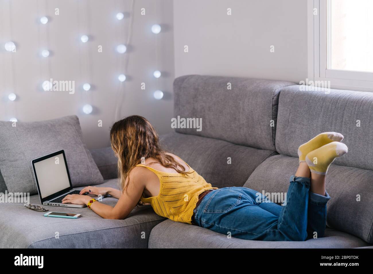 Blonde woman lying on sofa working with laptop at home Stock Photo - Alamy