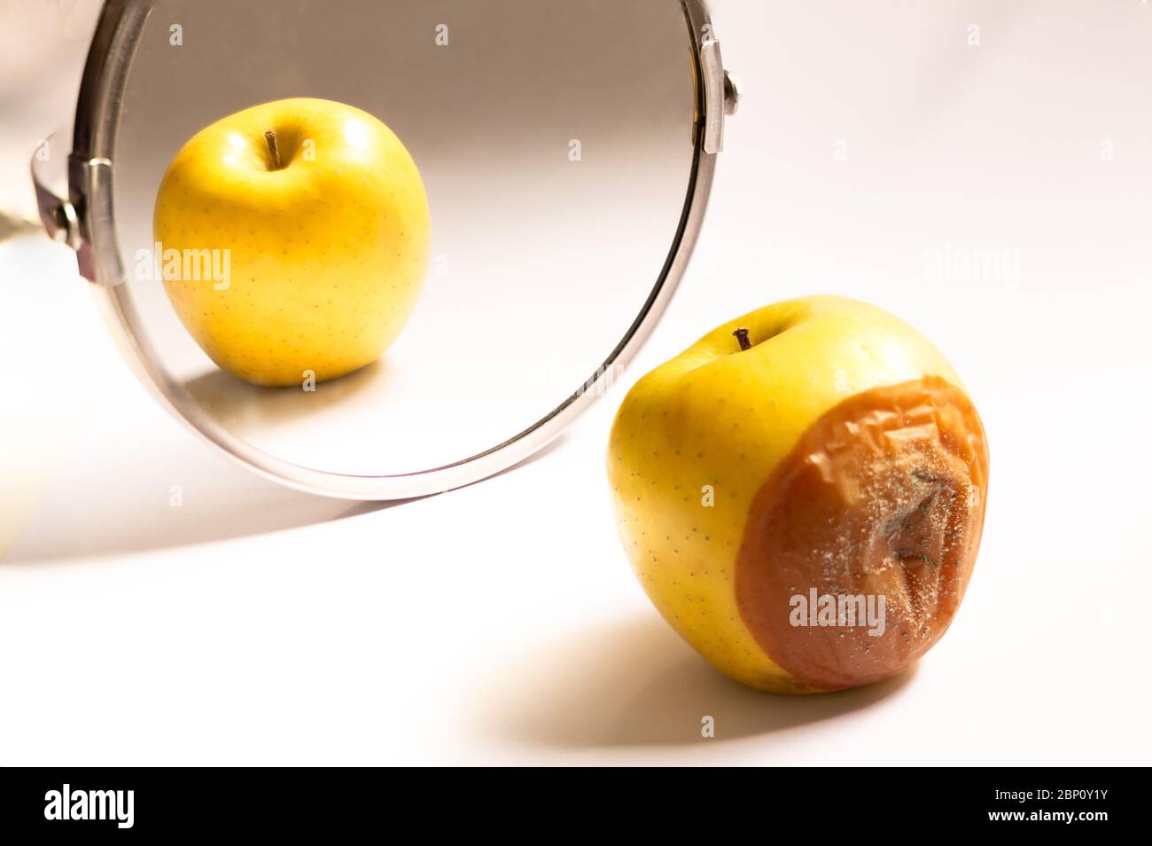 Apple in good condition looking at itself in the mirror while its back is rotten. Psychological concept, deception Stock Photo