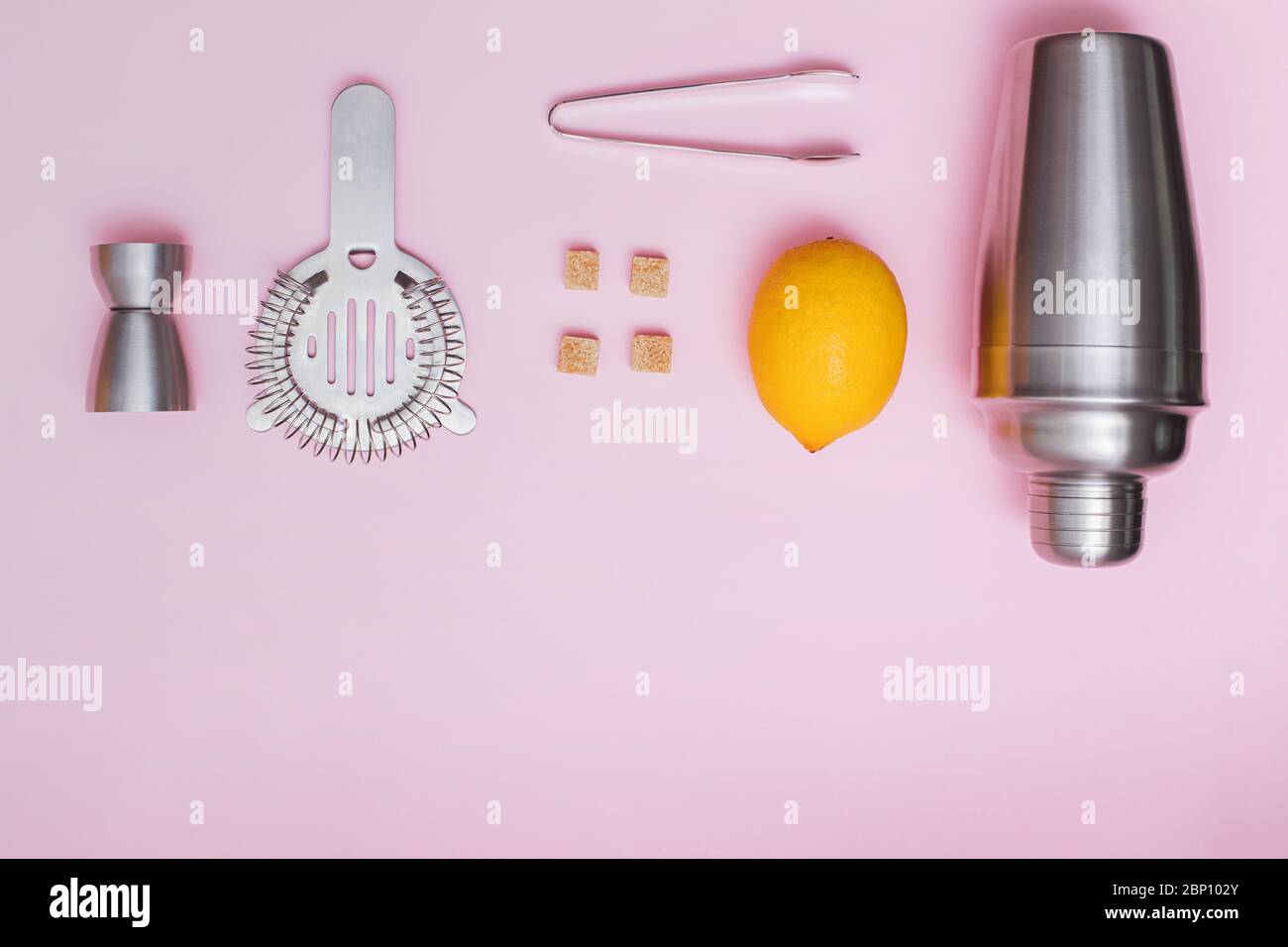 Shaker, jigger, and other bar tools with lemon and sugar on pink background Stock Photo