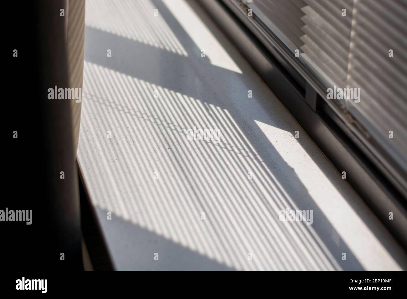 Shadow and light through blinds window on window sill. Morning light and shadow. Curtain on the left. Stock Photo