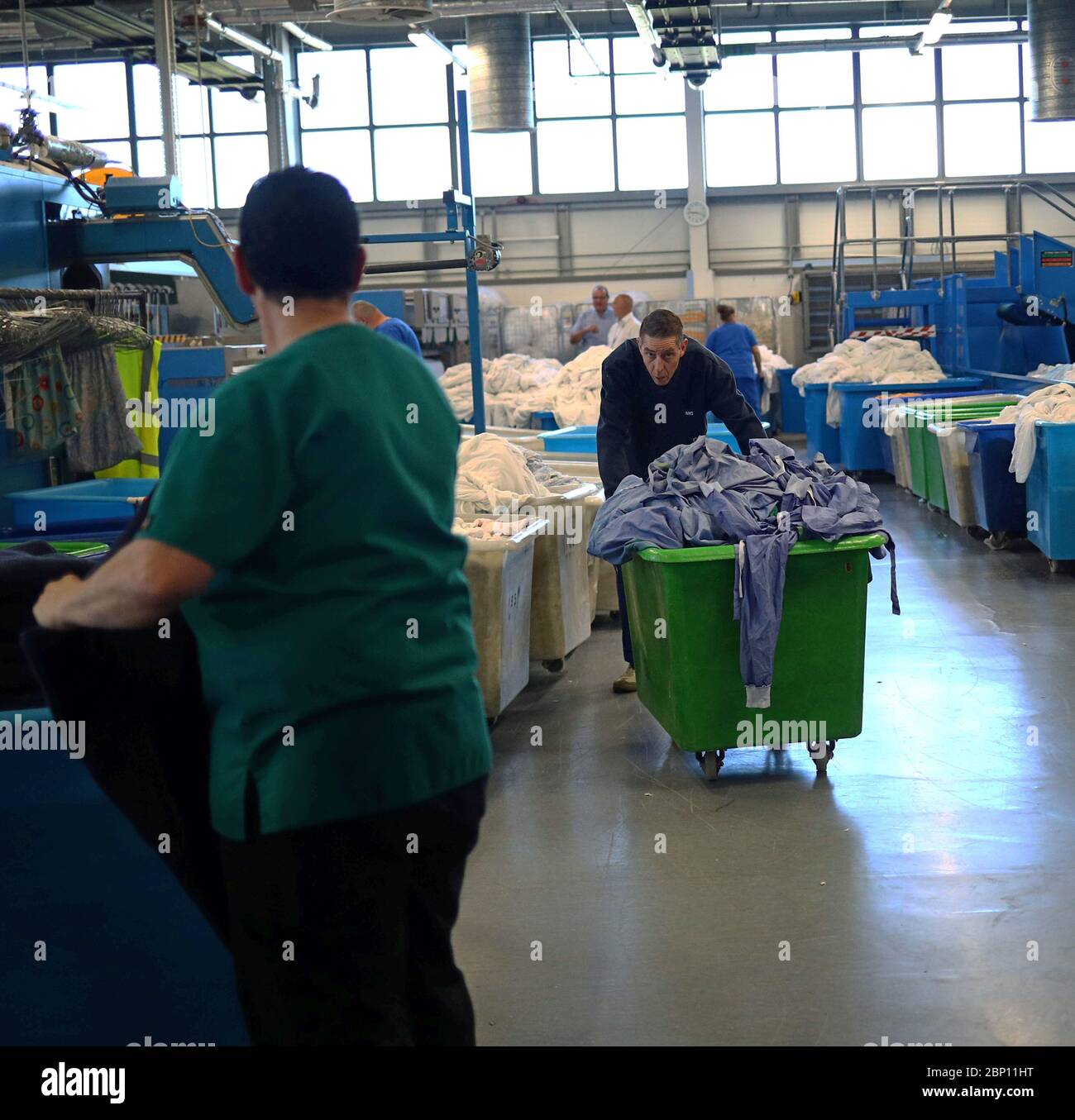 A laundry worker pushes a basket of gowns through the laundry and linen room at The Royal Blackburn Teaching Hospital in East Lancashire during the outbreak of the coronavirus disease. Stock Photo