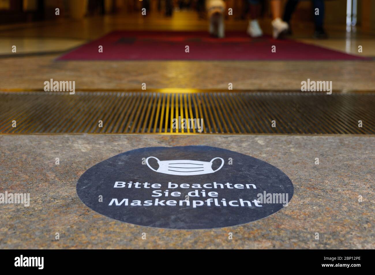 White face mask symbol and text with ' Bitte beachten Sie die Maskenpflicht ' means ' Please pay attention to the mask', sign on the floor in Germany. Stock Photo