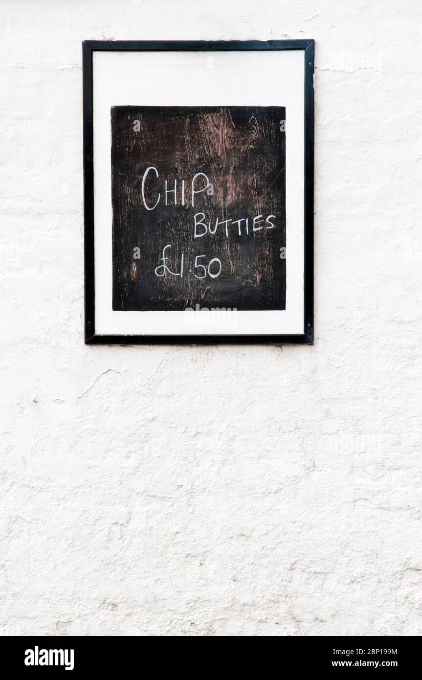 A Chip Butty Menu Hand Written In White On An Old Peeling Wooden Board Painted Black Stock Photo