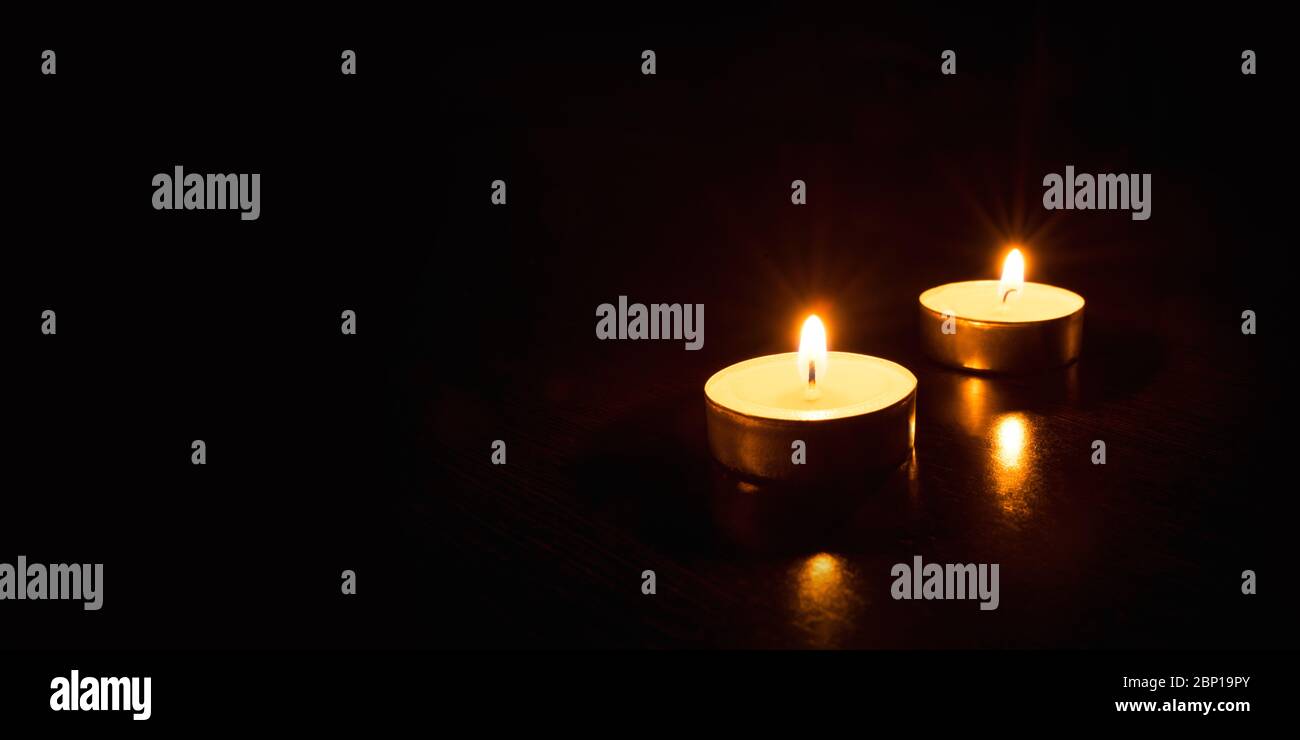 Two burning candles on a black background. Stock Photo