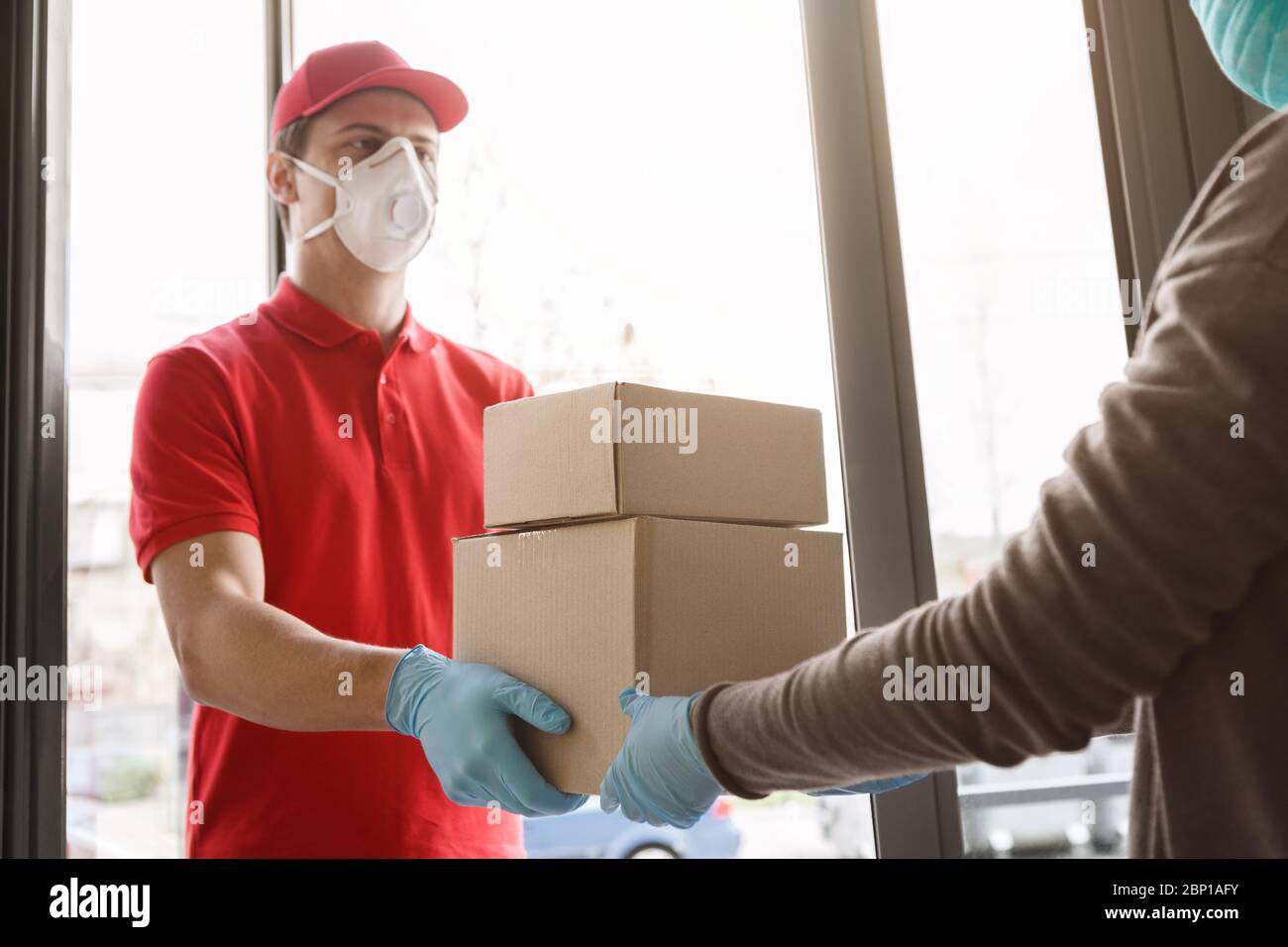 Receipt of parcel at home. Girl client meets courier and picks up parcel Stock Photo