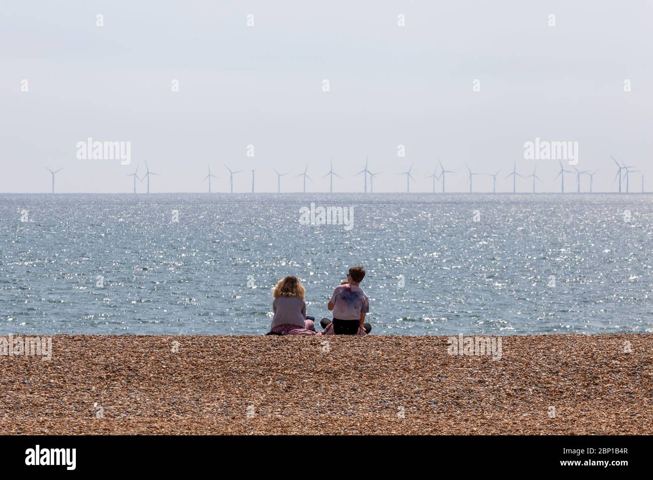couple sitting on beach with wind farm Stock Photo
