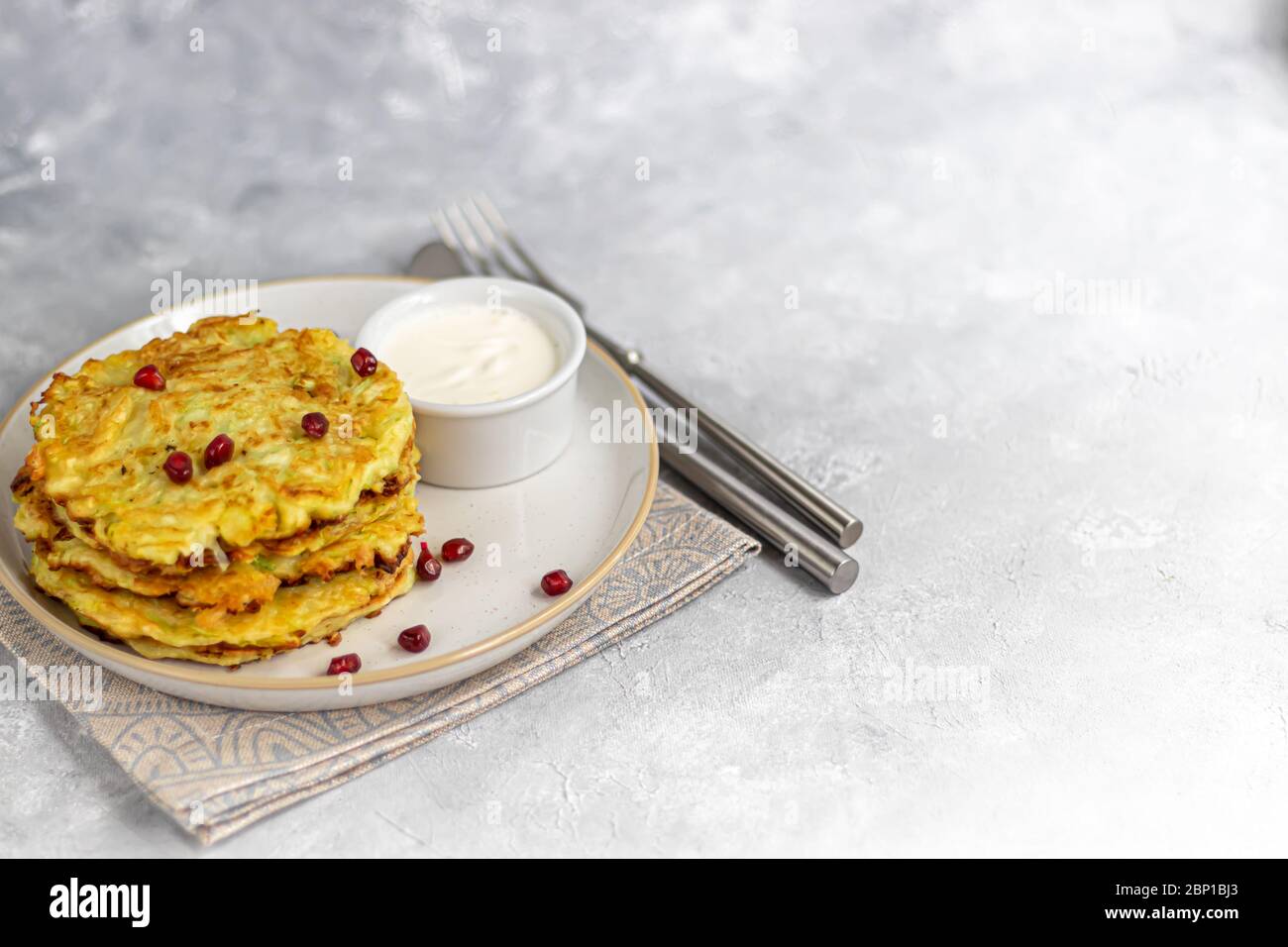 Zucchini fritters, vegetarian zucchini fritters, served with fresh herbs and sour cream. Garnished with strawberries and green onions. On a light gray Stock Photo