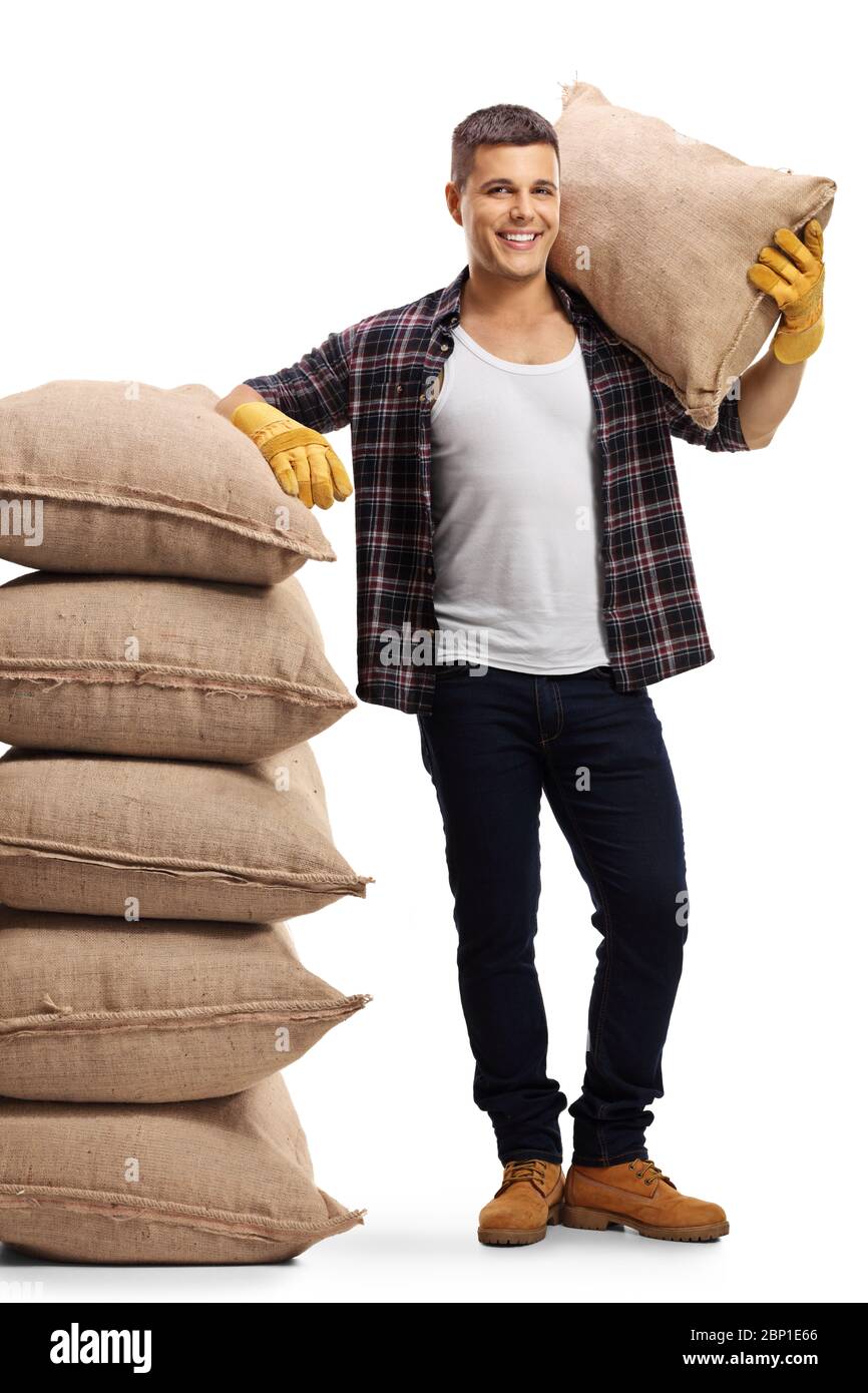 Full length portrait of a farmer leaning on a pile of sacs and holding a sack on his shoulder isolated on white background Stock Photo