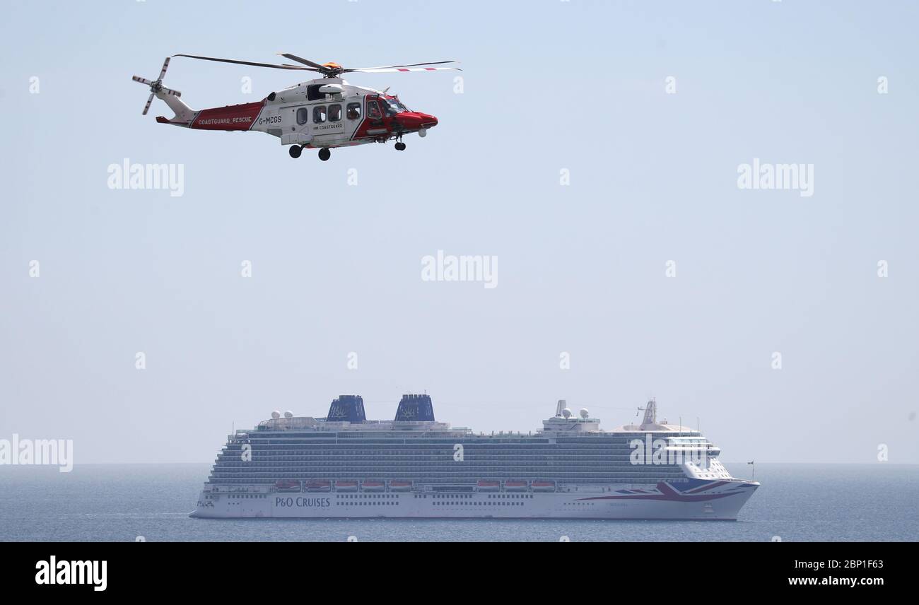 A helicopter from Her Majesty's Coast Guard flies over the P&O cruise ship Azura (right) and the Cunard cruise ship Queen Victoria at berth in Weymouth Bay. 6 ships, including 5 Cruise ships from P&O and Cunard and Cunard's Ocean Liner Queen Mary 2 have moored up in Weymouth Bay. 6 ships, including 5 Cruise ships from P&O and Cunard and Cunard's Ocean Liner Queen Mary 2 have moored up in Weymouth Bay whilst cruises are postponed or cancelled due to coronavirus. Stock Photo