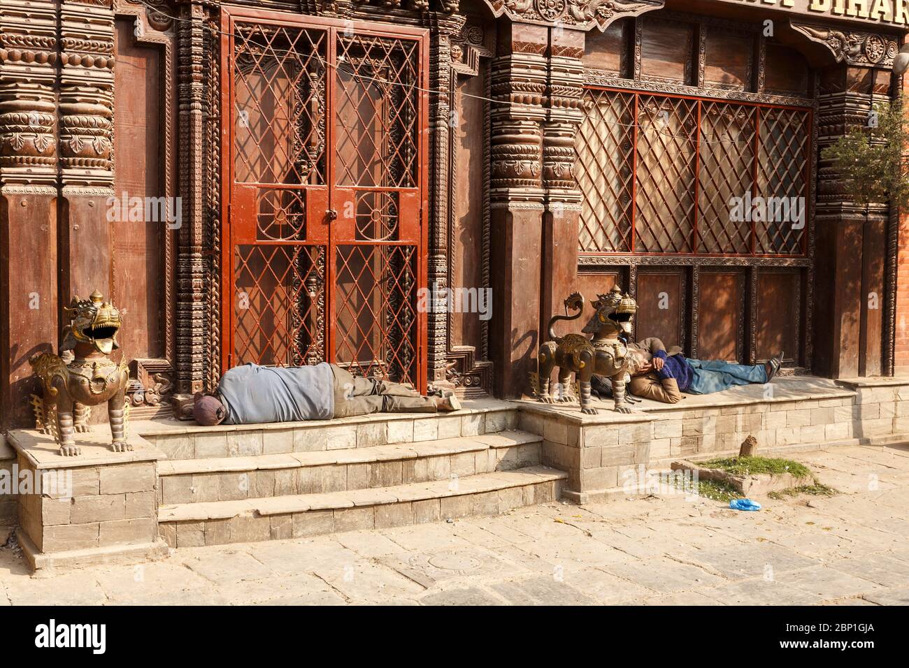 Kathmandu, Nepal - November 25, 2016: Two adult Nepalese men sleep on the steps in front of the temple entrance. Stock Photo
