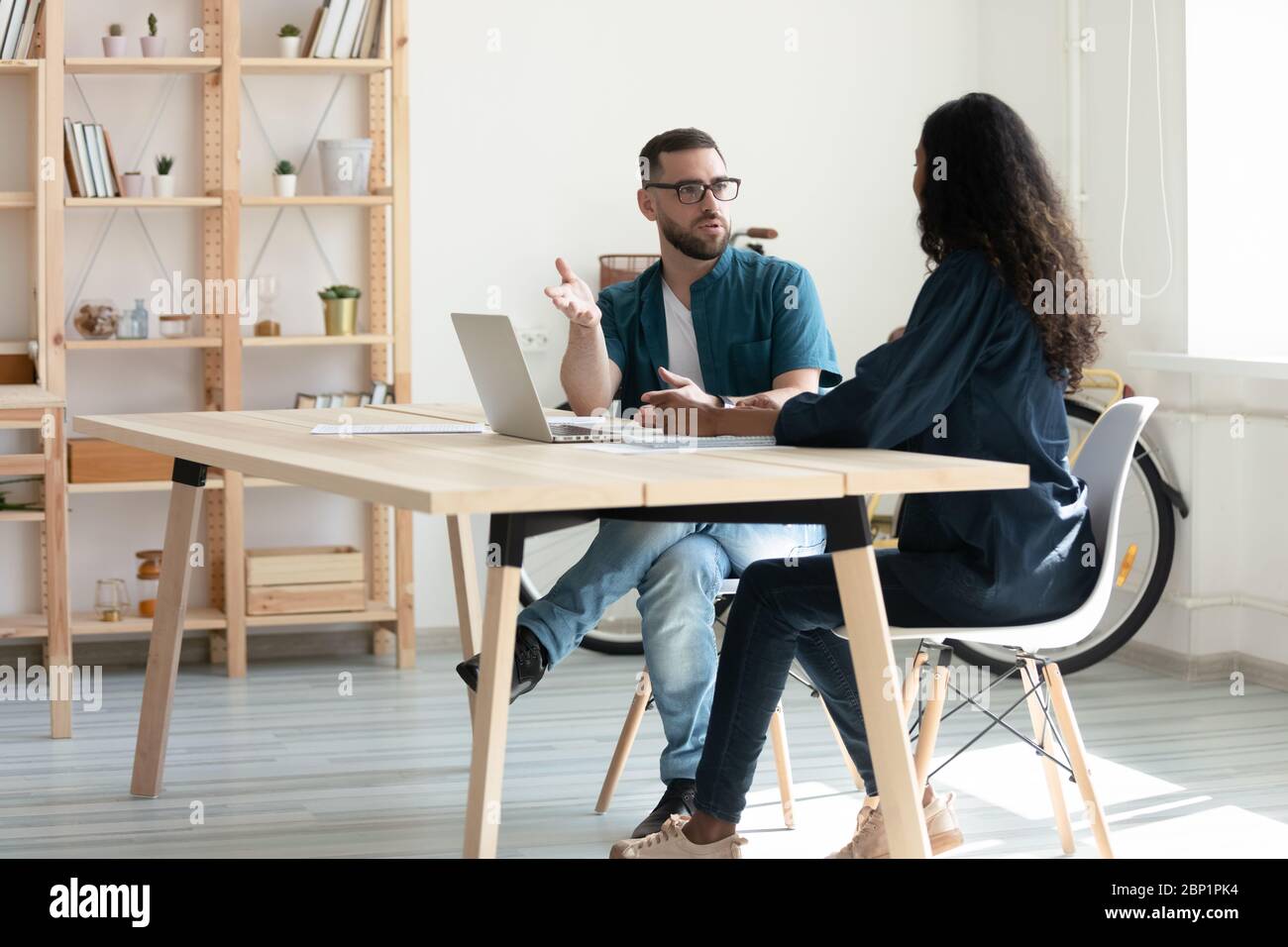 Confident bearded businessman talking with businesswoman using laptop in boardroom. Stock Photo