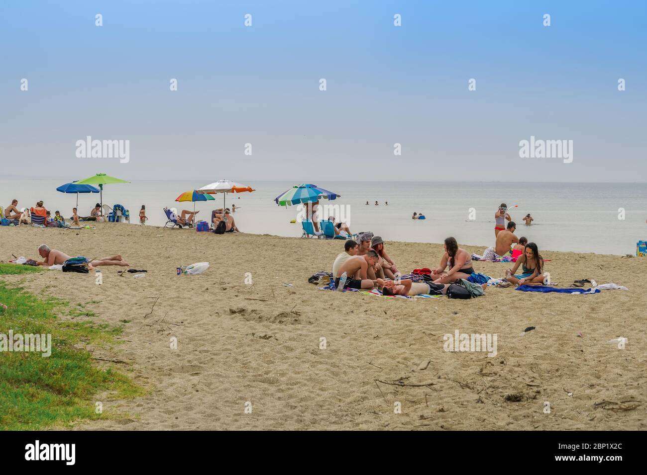 Neoi Epivates, Greece - May 16 2020: Public beaches open for the summer season. Bathers with sun umbrellas on sand by the sea at Thessaloniki suburbs, after government suggests people keep a distance. Stock Photo