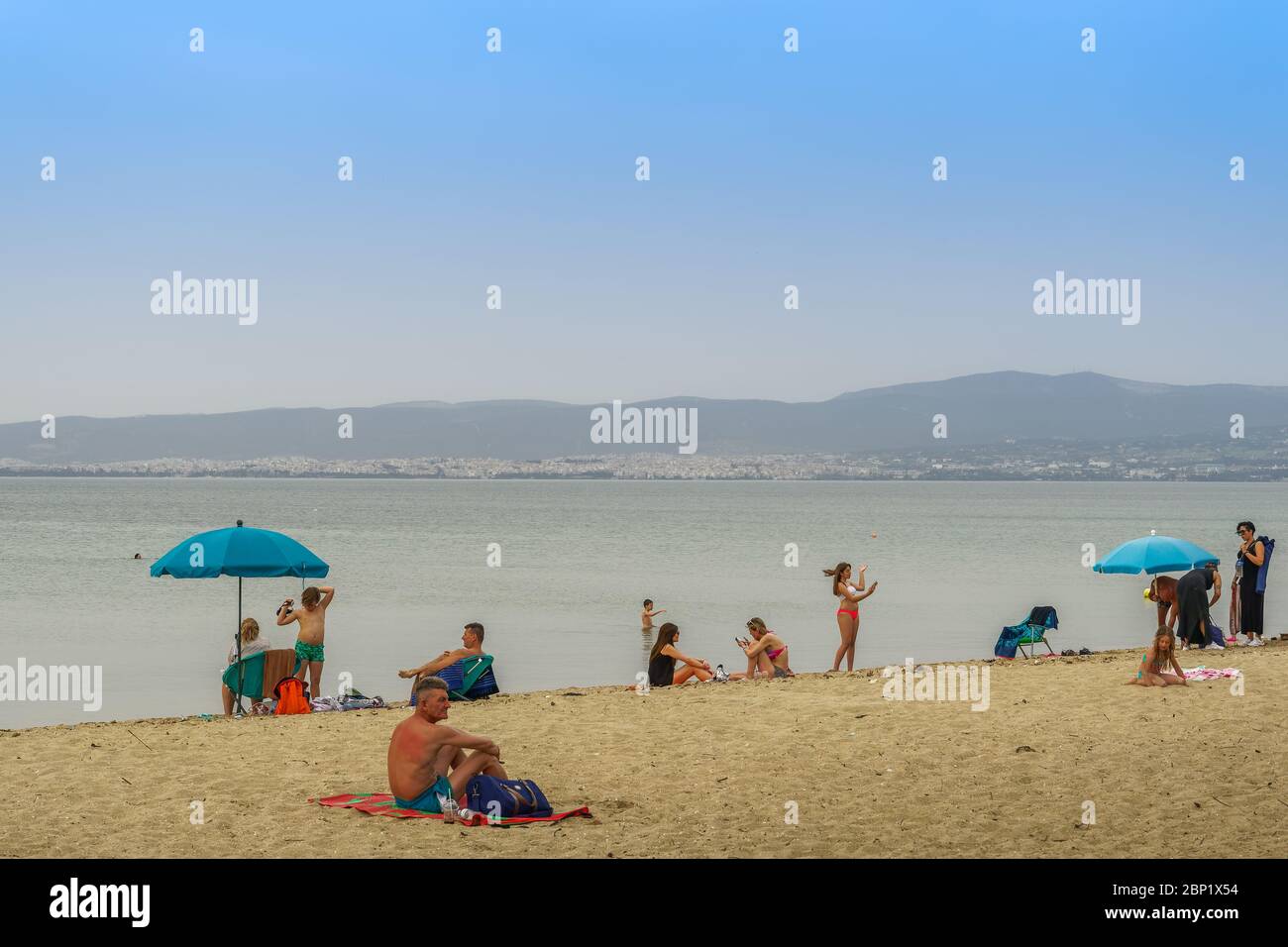 Neoi Epivates, Greece - May 16 2020: Public beaches open for the summer season. Bathers with sun umbrellas on sand by the sea at Thessaloniki suburbs, after government suggests people keep a distance. Stock Photo