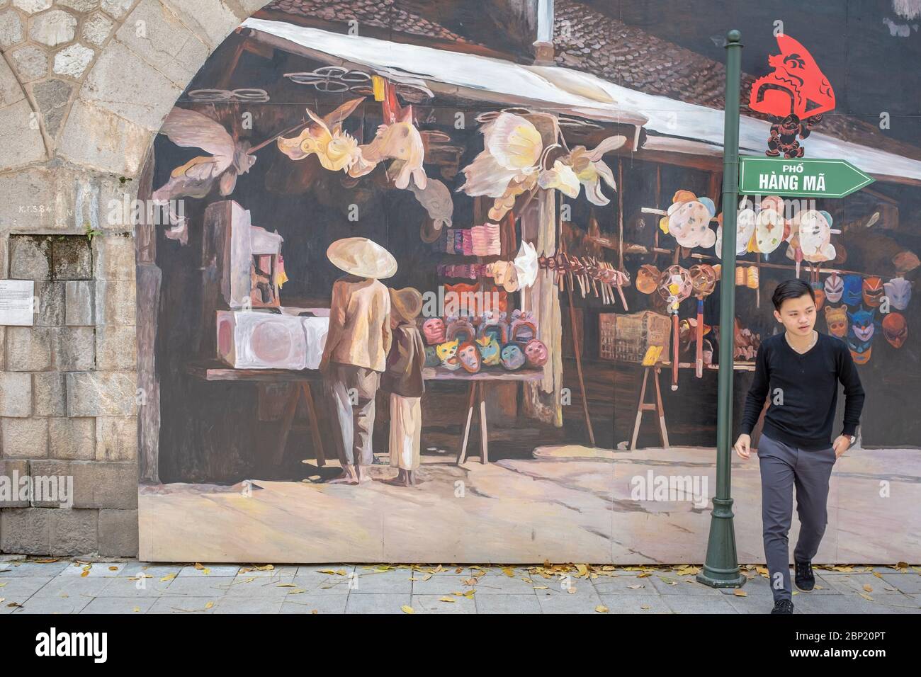 Hanoi, Vietnam - May 1, 2018: Young man walking away from a mural, seeming to walk out from the mural Stock Photo