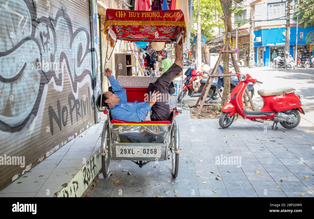 Hanoi, Vietnam - May 1, 2018: Older man napping on his pedal rickshaw, unaware of being photographed Stock Photo